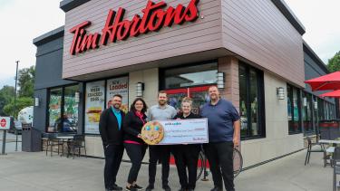 Smile Cookie Campaign 2023 Owners of Tim Hortons stand in front of Tim Hortons holding large cheque