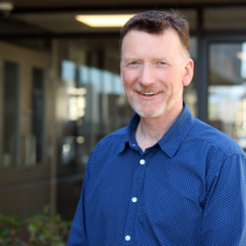 Man stands in front of building wearing a blue shirt