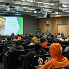 Large group of students gathered in large room in seats listening a speaker