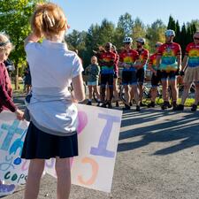 Tour de Valley group of riders standing in front of students who are holding signs.