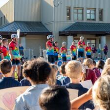 Students standing with the Tour de Valley riders stand and speaking in front of the student population.