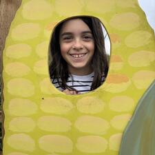 Smiling face of an elementary student who has placed their head into the cut out hole of the wooden corn cob.